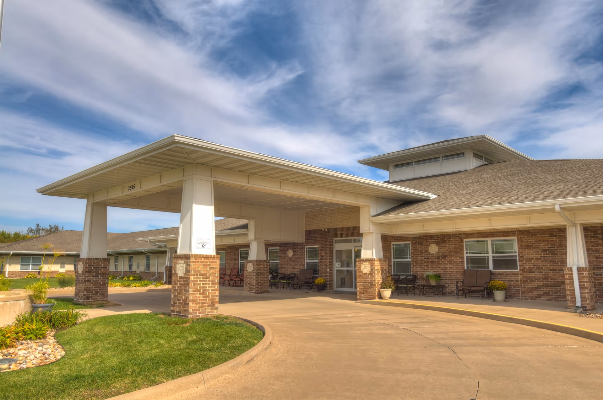 Covered drive-up entrance and portico of a brick senior living facility with seating under the overhang.