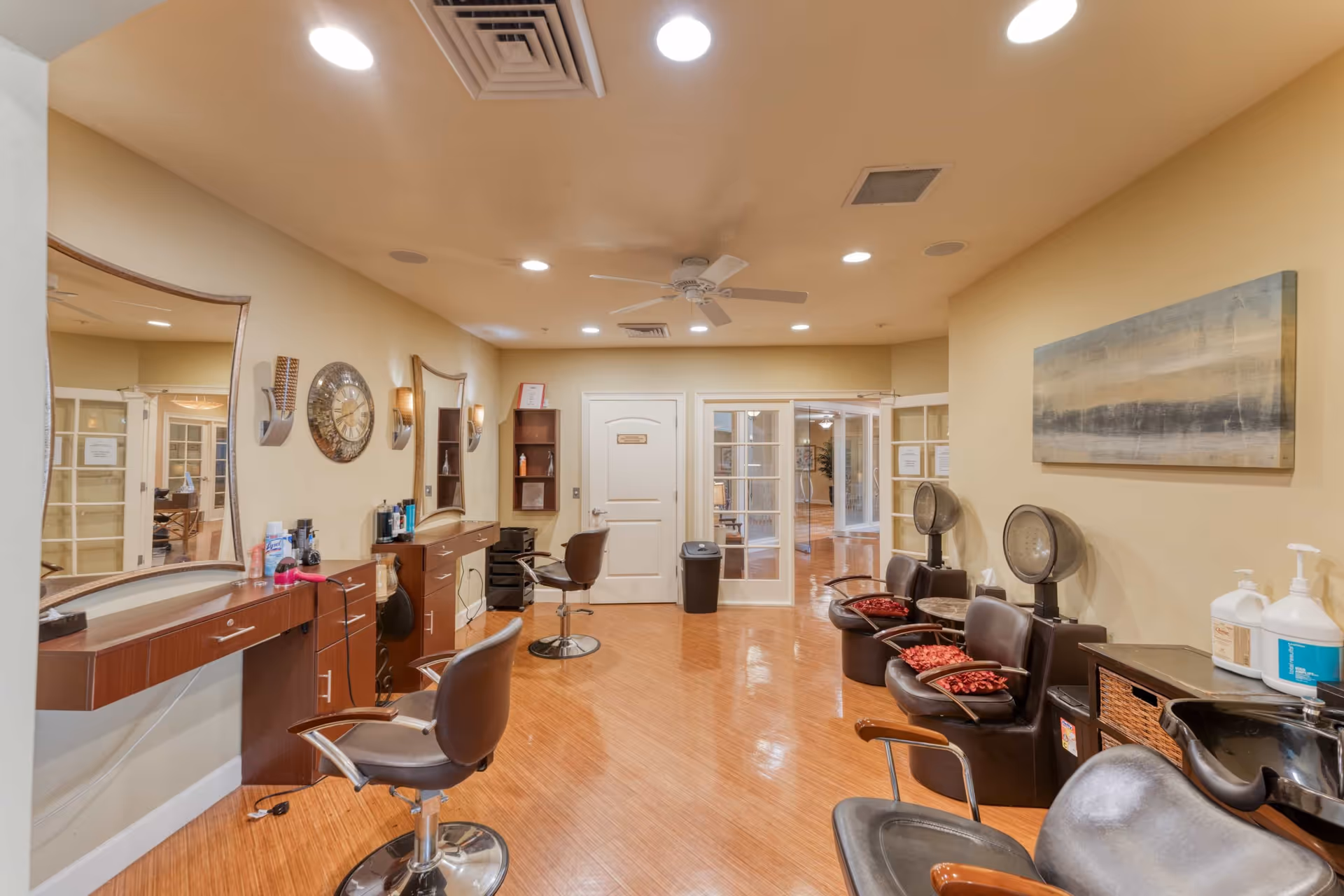 A bright salon interior with styling chairs, mirrors, hair dryers and cabinets in a senior living facility.