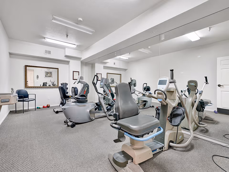 Small fitness room with several recumbent exercise bikes and a mirrored wall.