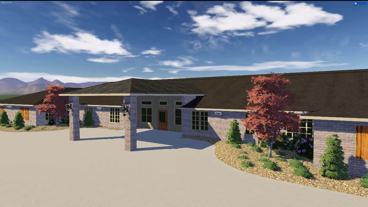 Front entrance of a single-story brick assisted living building with a covered porte-cochere and landscaped beds under a partly cloudy sky.