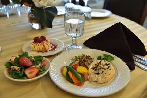 A plated meal with an entrée, colorful vegetables, a side salad, dessert, and a glass of water on a set dining table.