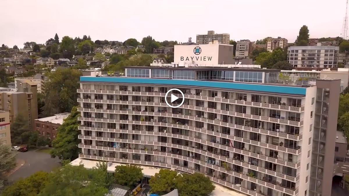 A large multi-story building with numerous balconies, identified as Bayview Retirement Community, surrounded by trees and other residential buildings in the background.
