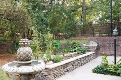 Outdoor courtyard featuring a stone raised garden bed, fountain, brick wall and greenery.
