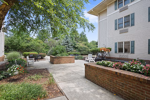 Sunlit courtyard with brick planters, patio chairs, and landscaping beside a multi-story building.