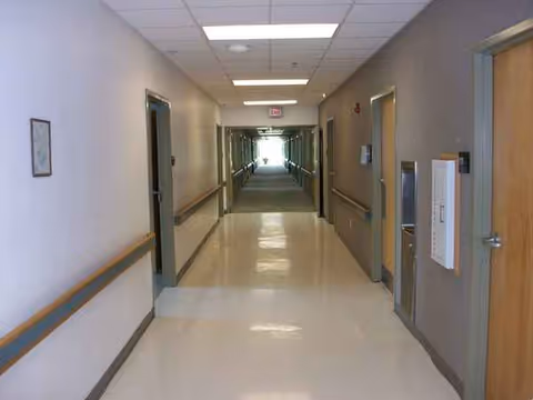 Long, well-lit interior hallway of a nursing home with doors on both sides.