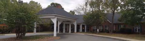 Exterior view of Cleveland House senior living facility with a covered entrance and trees.