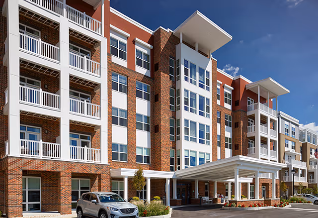 Multi-story brick senior living building with balconies, a covered entrance canopy, and a parked car in front.