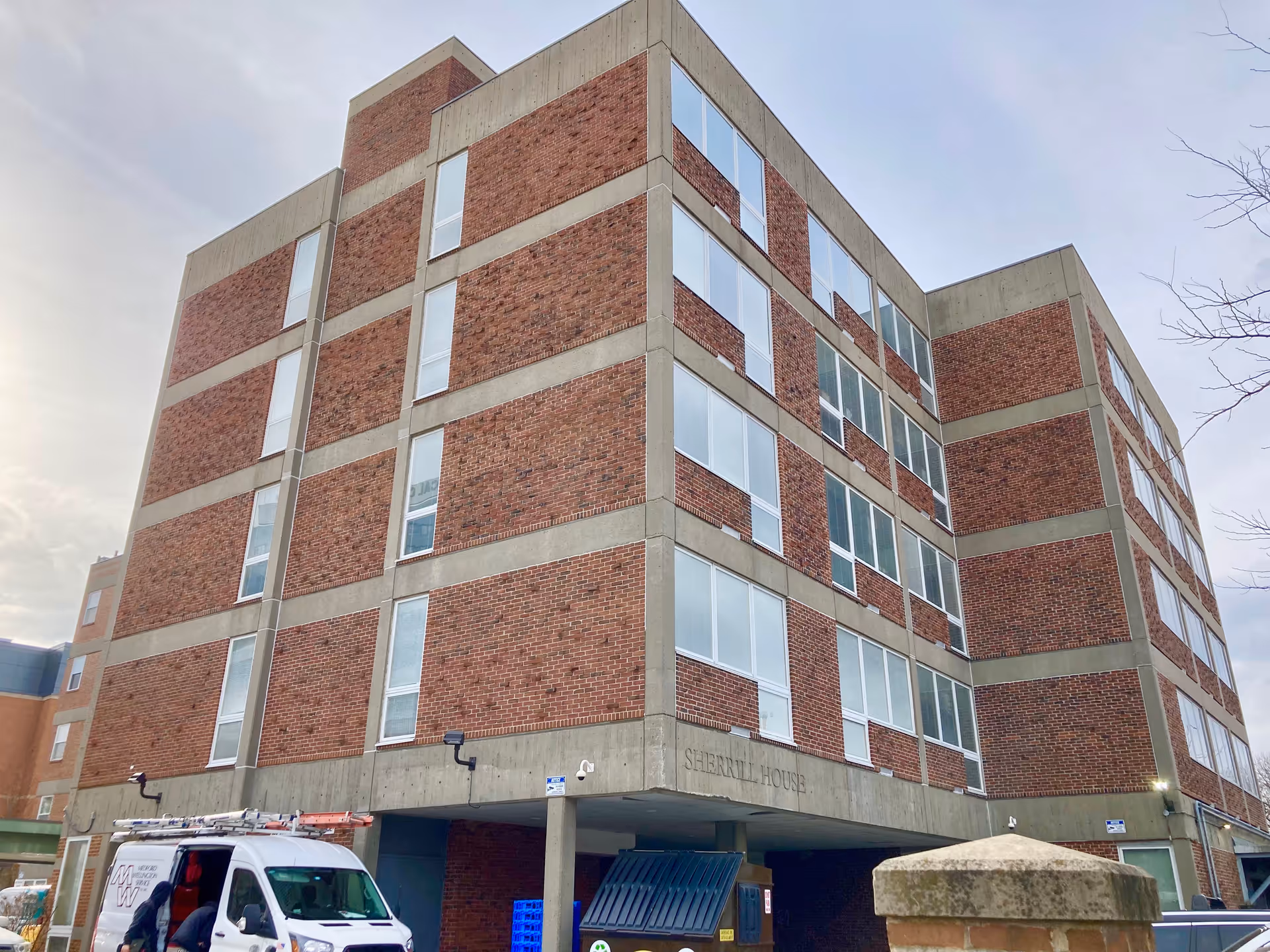 Multi-story brick and concrete building labeled "Sherrill House" with a covered entrance and a van parked in front.