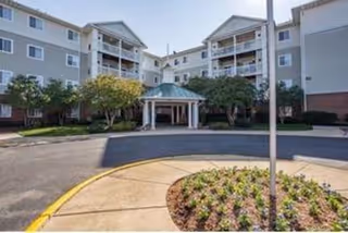Front entrance and circular driveway of a multi-story senior living building with a covered porte-cochere and balconies.