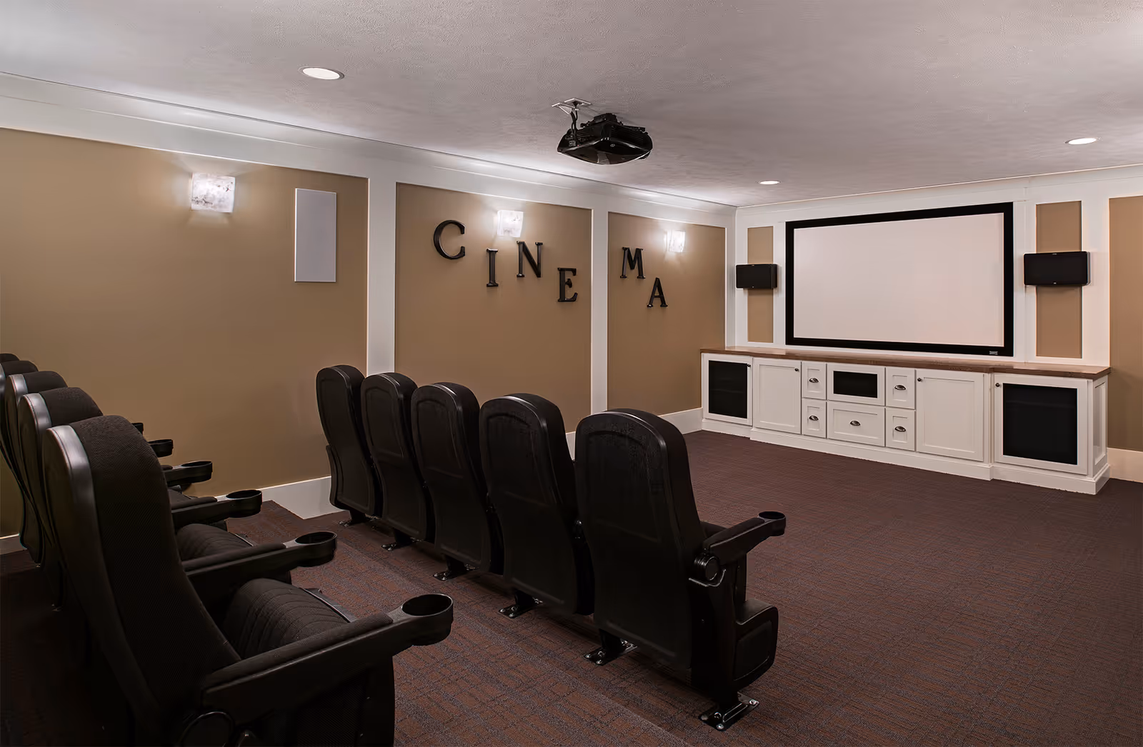 Small private cinema room with two rows of black theater seats facing a large projection screen and wall-mounted speakers.