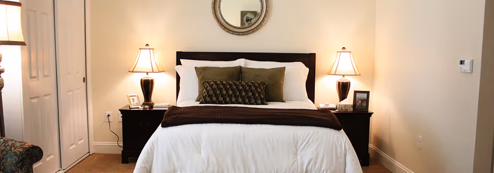 A neatly made bed with pillows and a dark headboard flanked by two bedside tables and lamps in a bedroom.