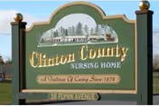 Green and gold Clinton County Nursing Home entrance sign with trees in the background.
