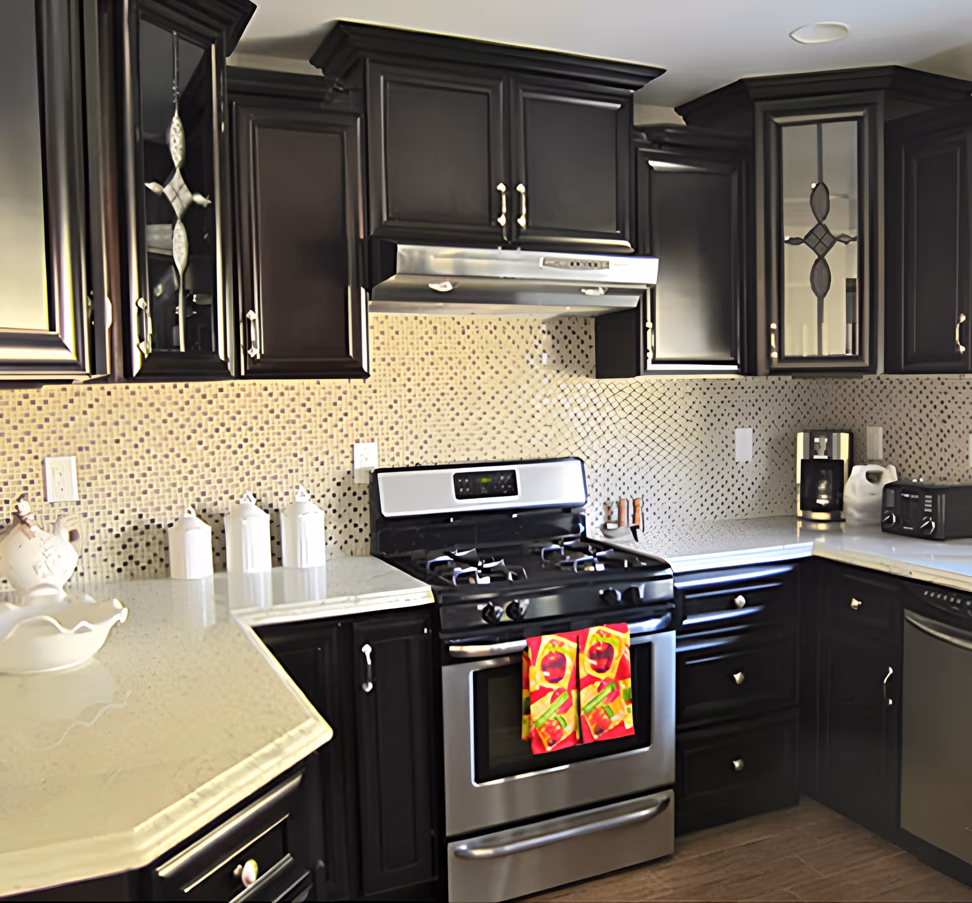 Modern kitchen with dark cabinets, a stainless steel gas stove and oven, mosaic tile backsplash, and light countertops.