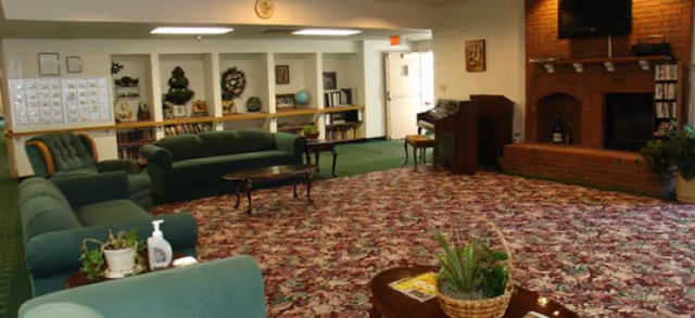 Carpeted communal lounge with green sofas, coffee tables, bookshelves and a brick fireplace.