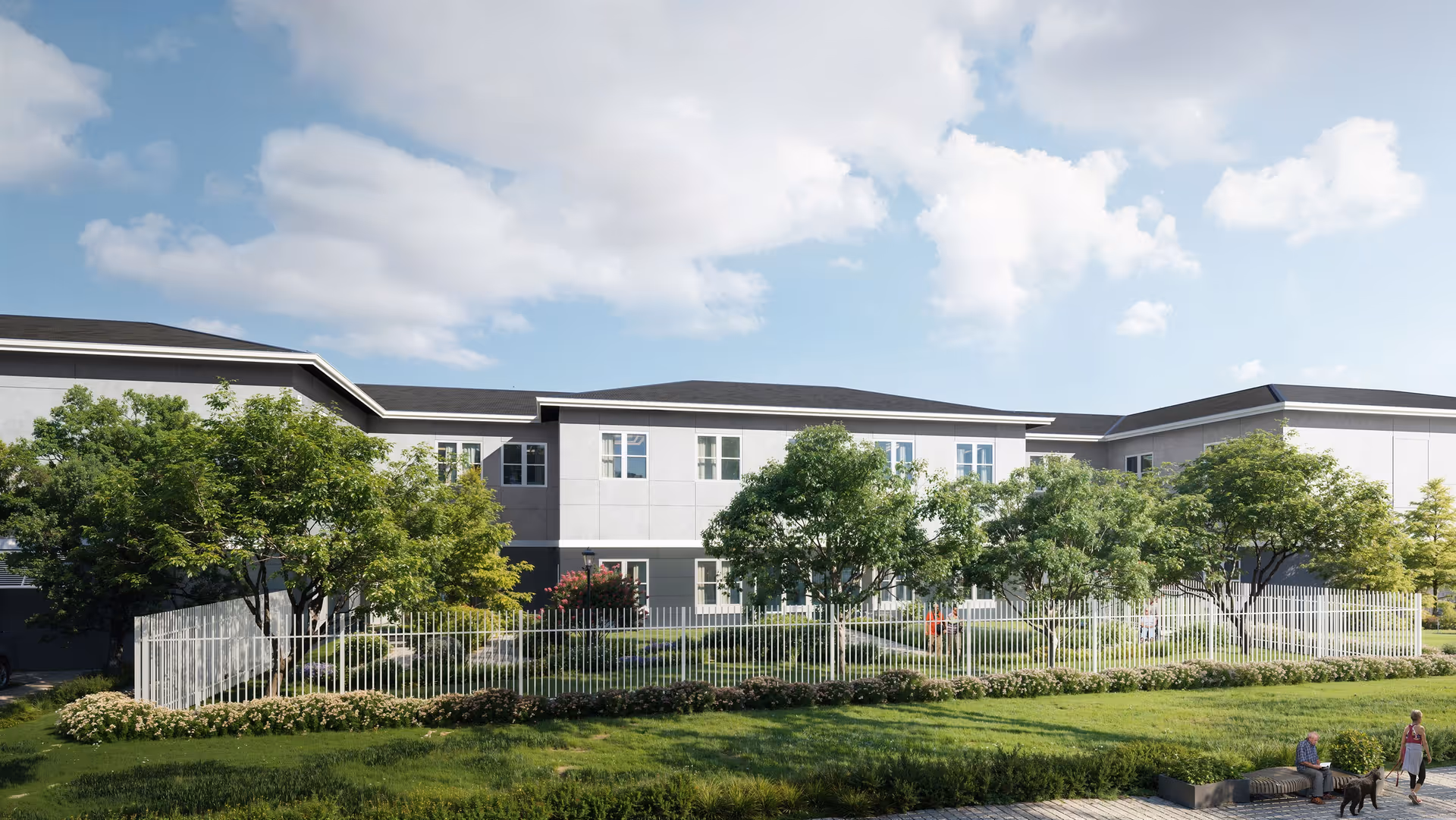 Exterior view of a two-story senior living building with a fenced landscaped yard, trees, and people walking nearby.