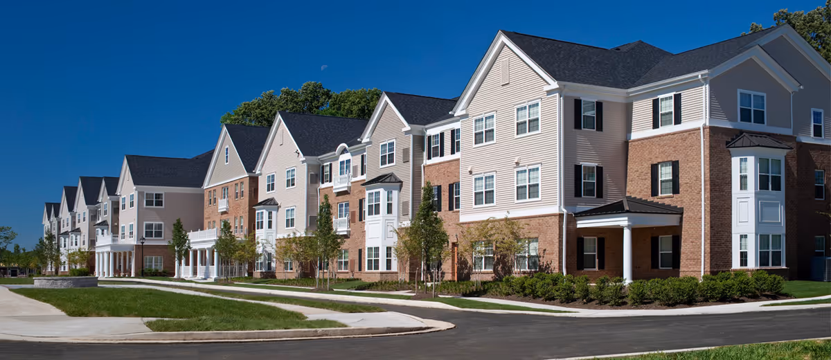 Row of modern senior apartment buildings with brick and beige siding along a curved street.