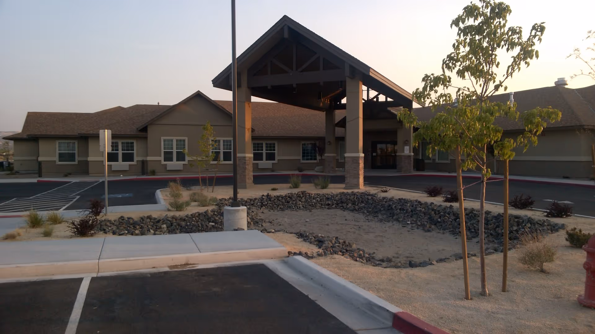 Front entrance of a single-story senior living building with a covered porte-cochère, parking area, and desert landscaping.