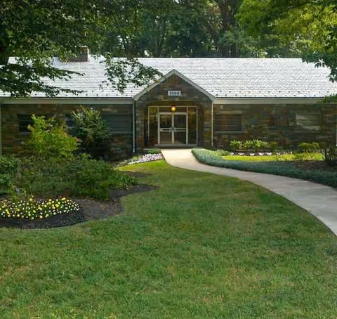 Front entrance of a stone nursing home with a curved walkway and manicured lawn.