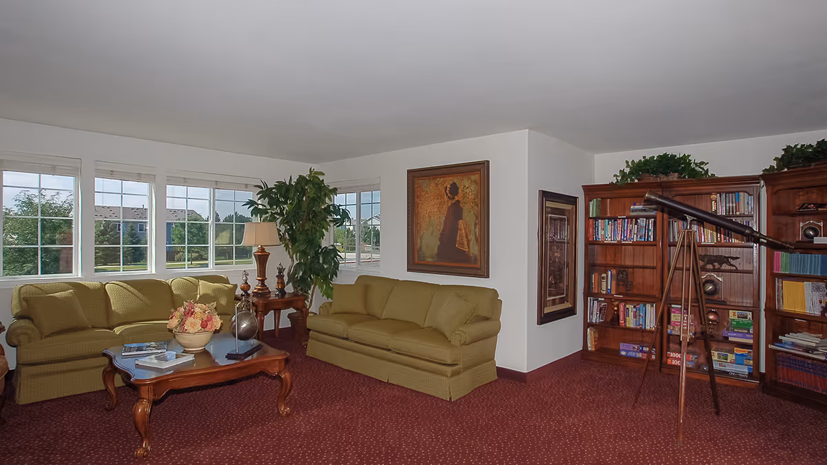 Bright living room with green sofas, a wooden coffee table, bookshelves and a telescope beside large windows.