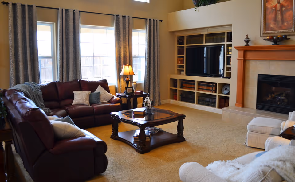 Bright living room with leather sofas, a coffee table, built-in shelving and TV, and a fireplace.