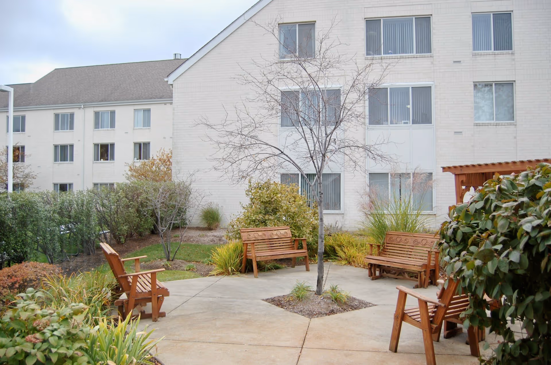 Courtyard with wooden benches and a small leafless tree in front of a multi-story residential building.