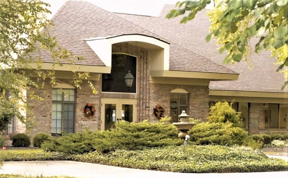 Brick building front with an arched entrance, double doors, landscaping and a small fountain in the foreground.