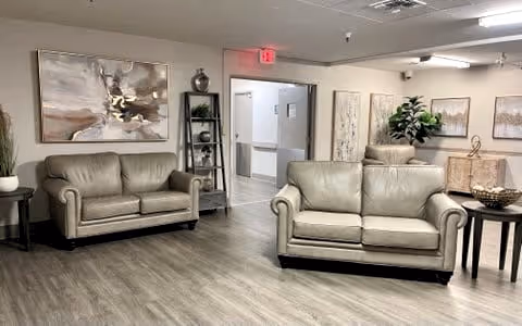 A communal lounge with two gray leather sofas, side tables, artwork, and a hallway entrance.