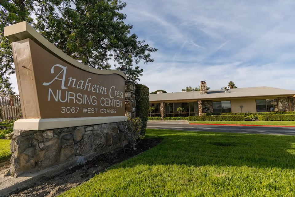 Stone entrance sign for Anaheim Crest Nursing Center with the one-story facility and lawn in the background.