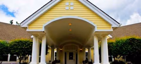 Yellow building with white columns and a curved portico at the entrance.