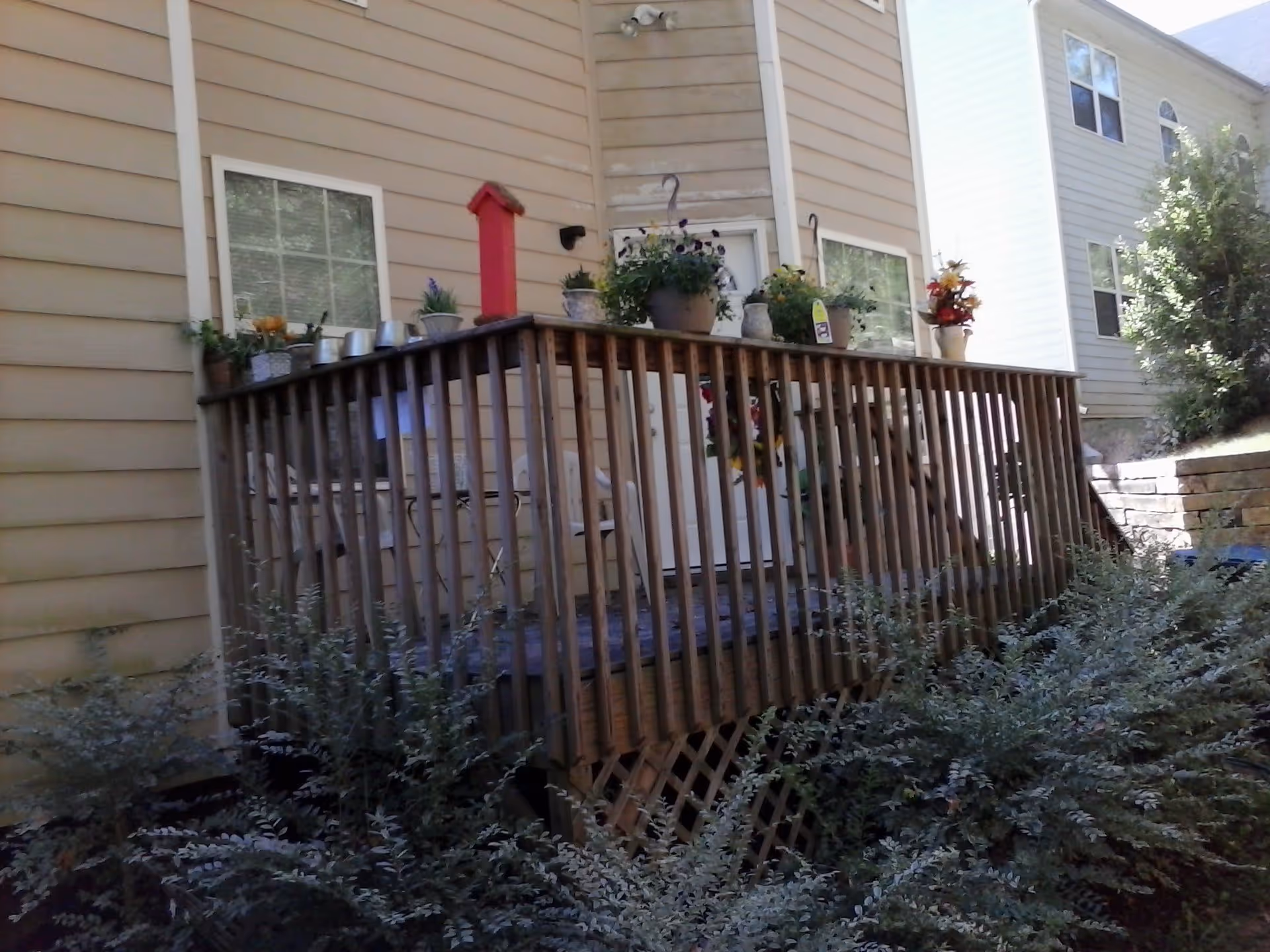 Wooden exterior deck with railing and potted plants attached to a beige-sided house.