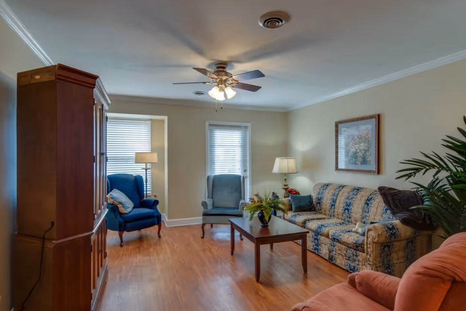 Living room with a patterned sofa, armchairs, coffee table, and a ceiling fan.