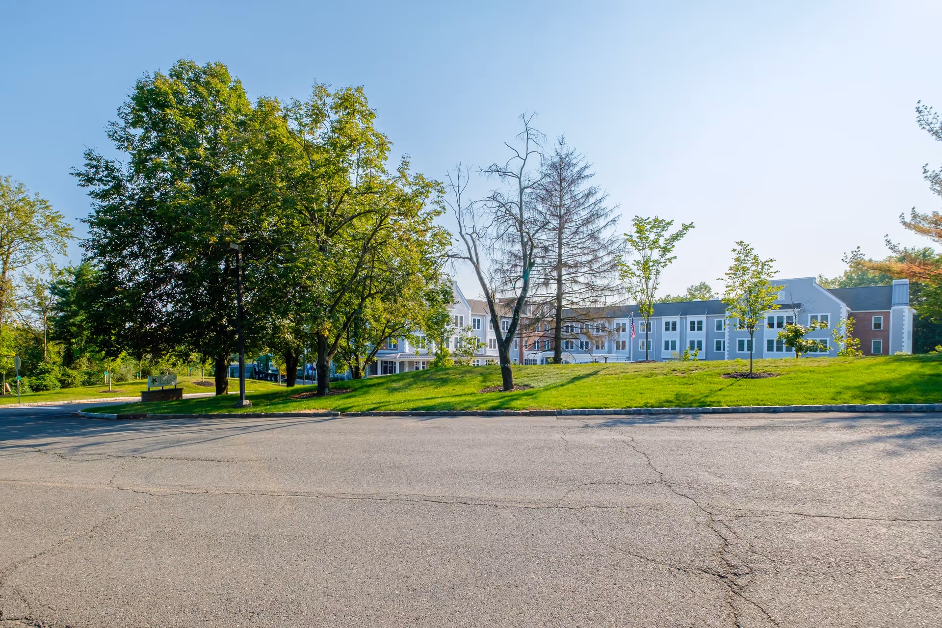Front exterior of a multi-story senior living residence with a grassy lawn and trees under a clear sky.