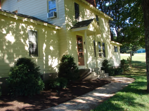 Exterior view of a pale yellow senior living facility with a front door and steps.