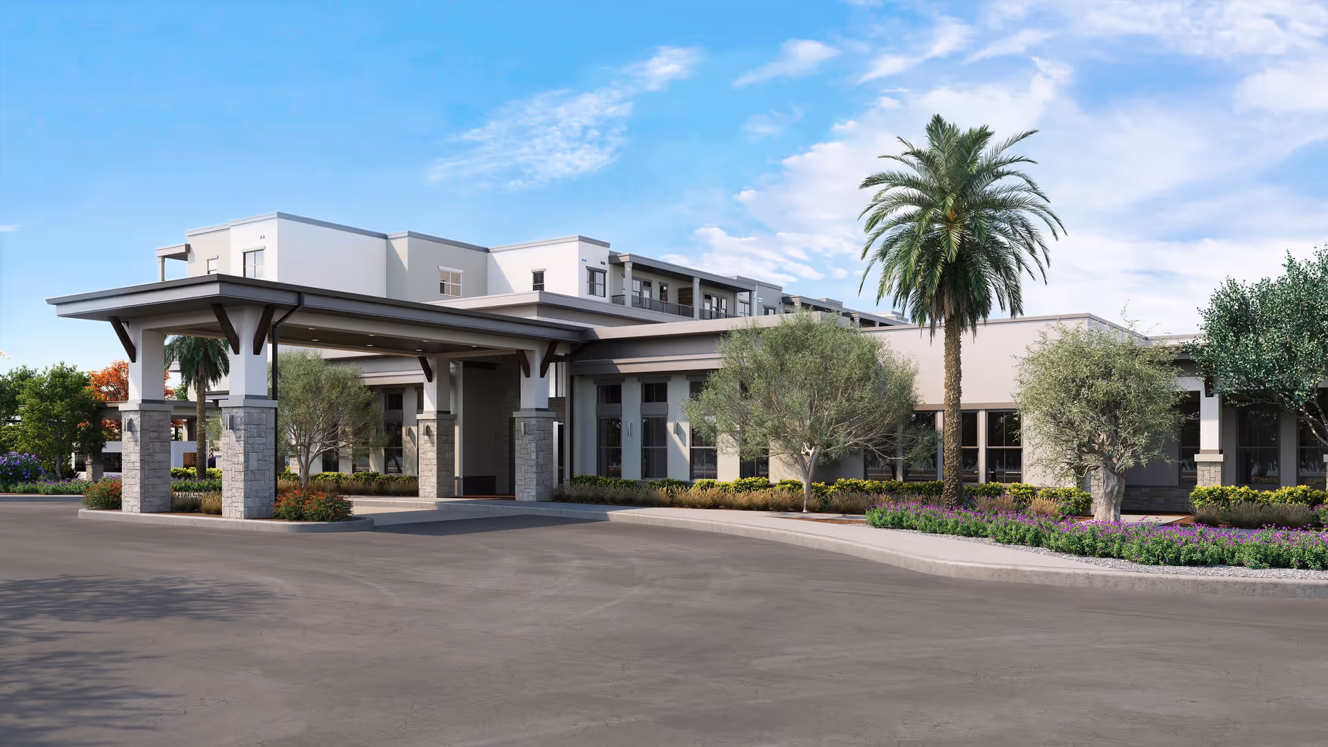 Exterior view of Amberlin Arrowhead senior living facility showing a modern building with a covered entrance supported by stone pillars, surrounded by landscaped greenery including palm trees and shrubs under a blue sky with some clouds.