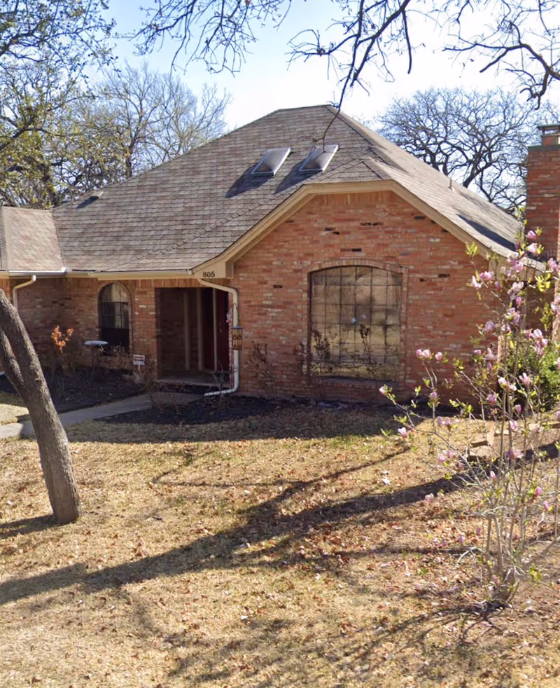 Brick residential care home with front entrance, lawn, and blooming tree.