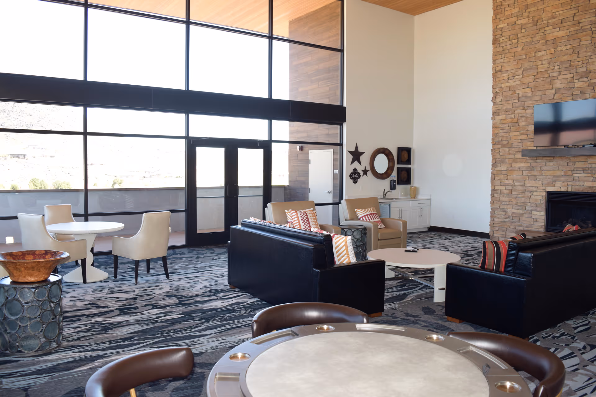 Bright senior living lounge with floor-to-ceiling windows, sofas and chairs arranged around a coffee table and fireplace.