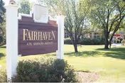 A landscaped front lawn with trees and a wooden sign reading "Fairhaven" and the building behind it.