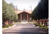 Driveway lined with American flags leading to the front entrance of a brick building framed by trees.