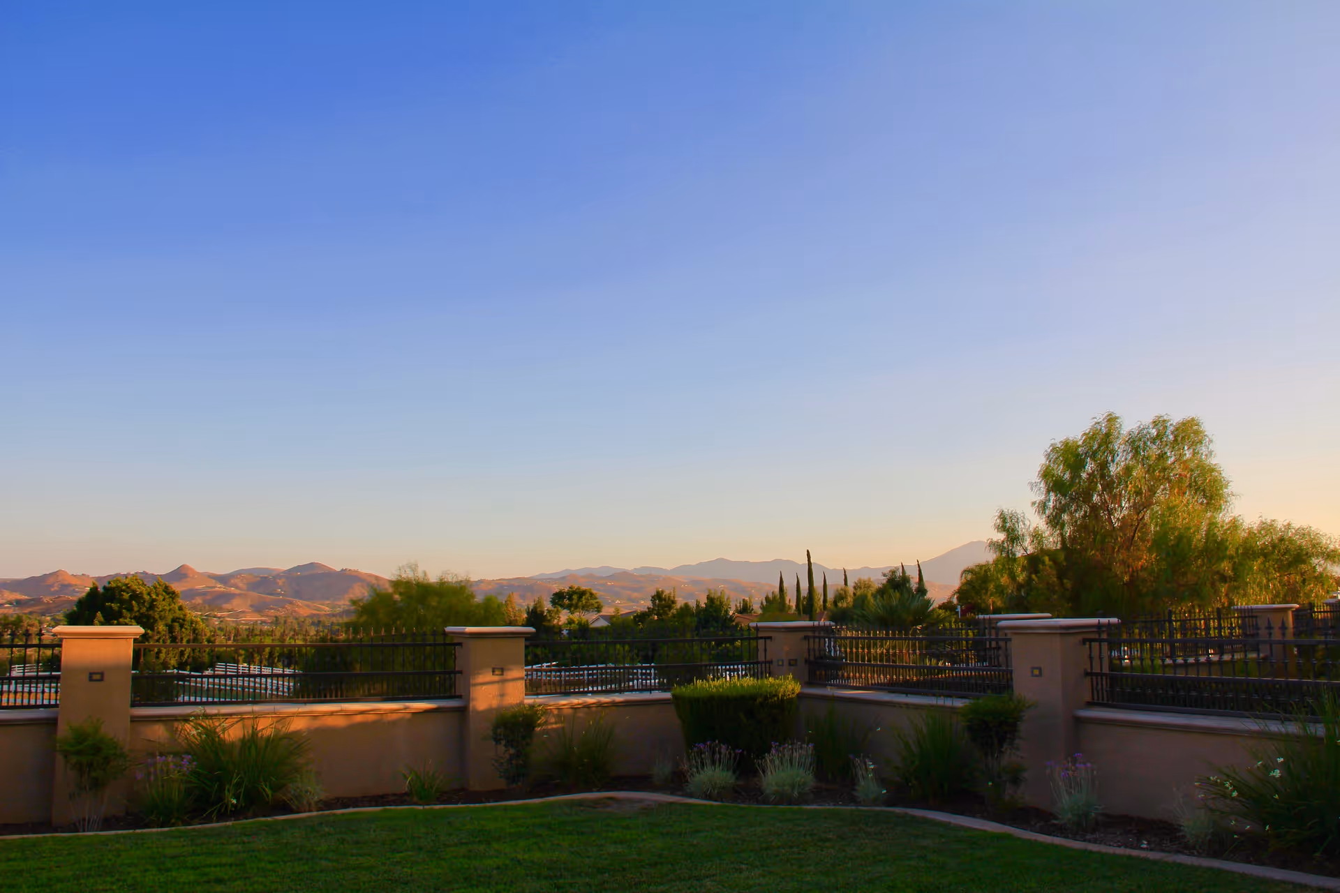 View over a walled courtyard and garden toward distant hills under a clear blue sky.