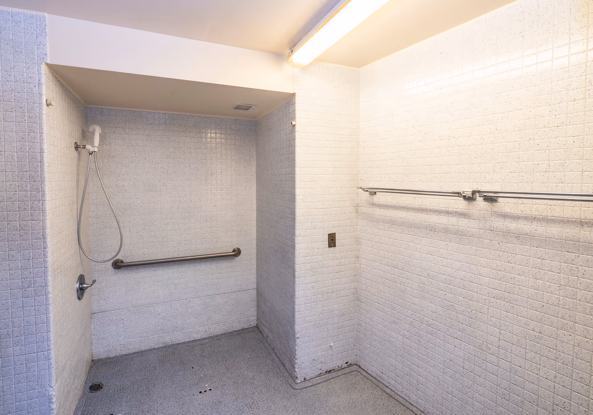 Accessible tiled shower room with a handheld showerhead, horizontal grab bar, and wall-mounted towel bars.