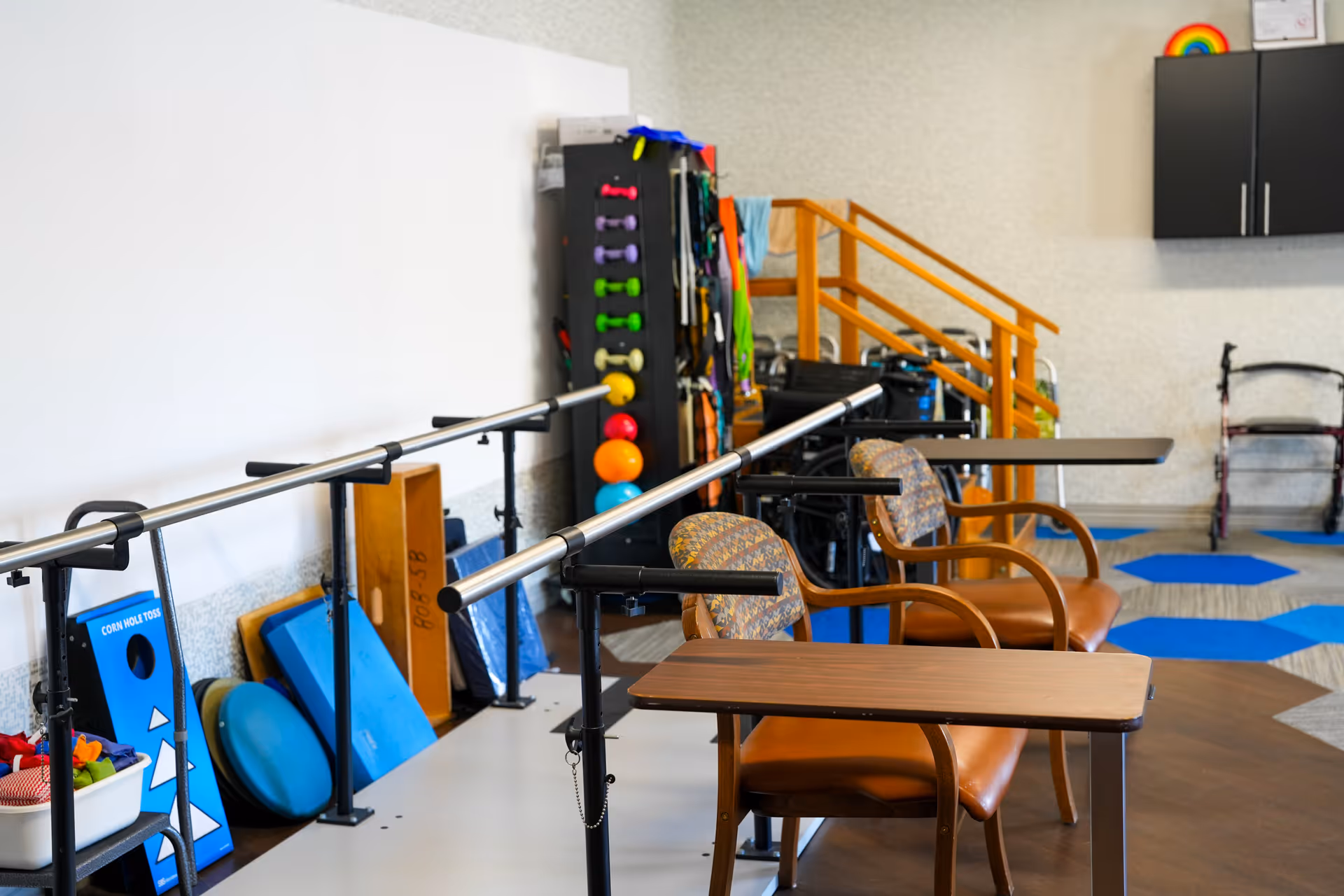 Therapy/rehab room with parallel bars, chairs, and various exercise equipment and therapy props.