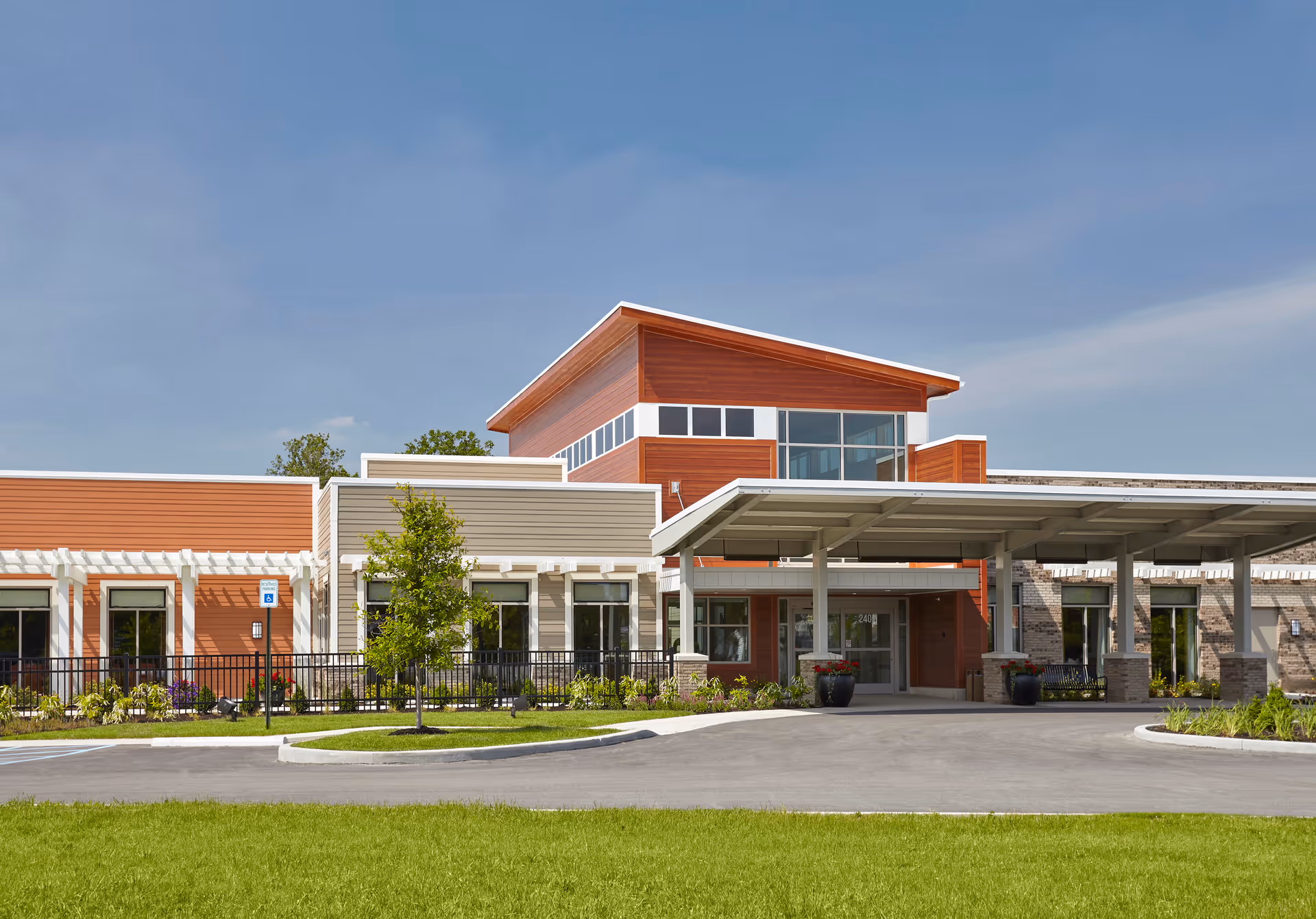 Modern senior living facility front entrance with a covered porte-cochère, large windows, and landscaped lawn.