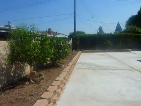 Outdoor paved area with a concrete driveway, brick edging, and garden beds.