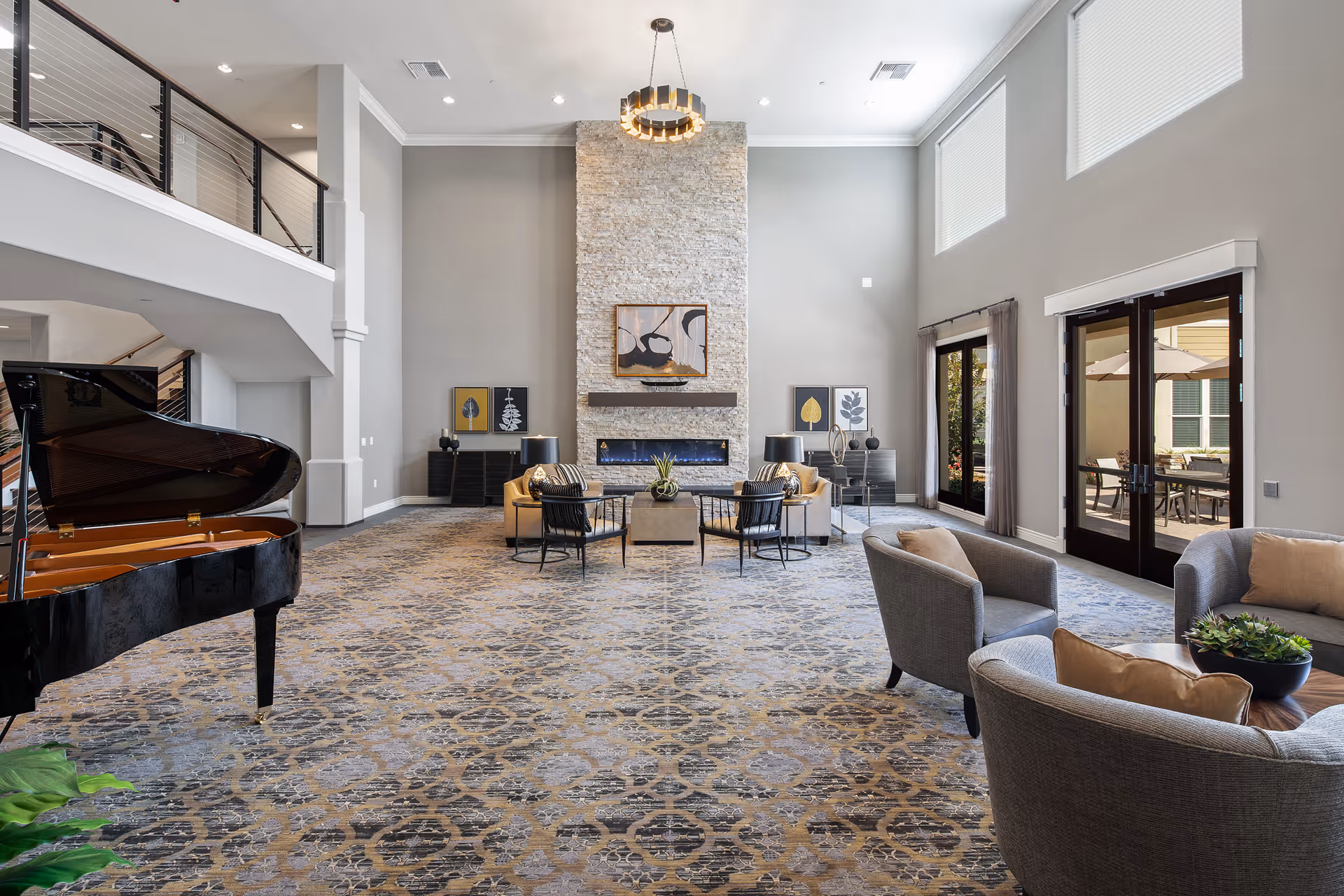 Spacious, sunlit community lounge with high ceilings, a grand piano, multiple seating areas, and a central stone fireplace.