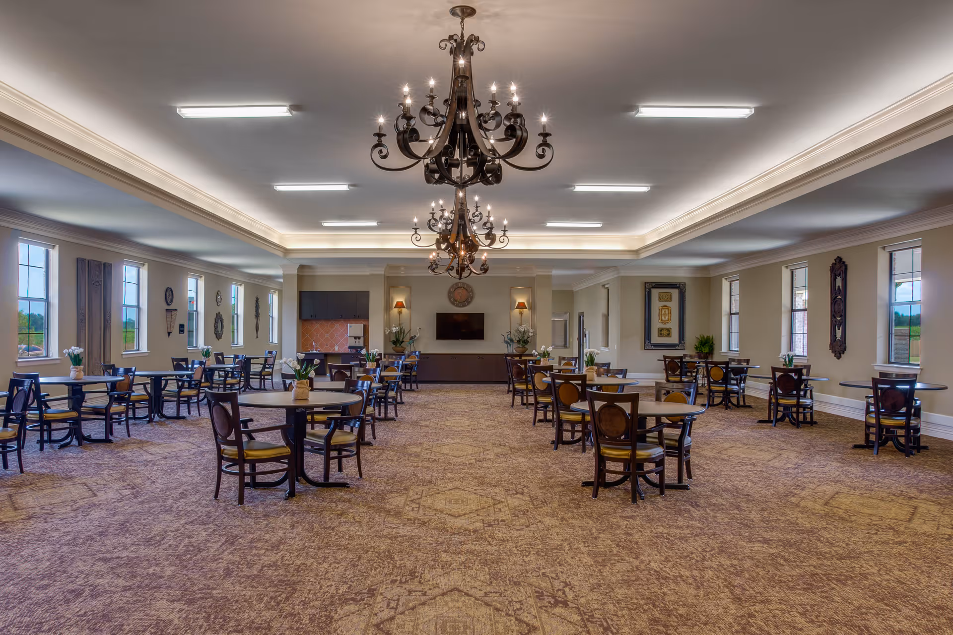 Spacious dining room with round tables and chairs, large windows, and ornate chandeliers.