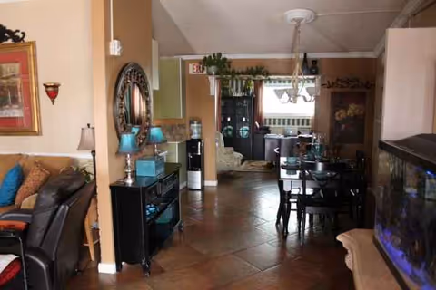 Open living area with seating, dining table, chandeliers, and plants in a senior living facility.