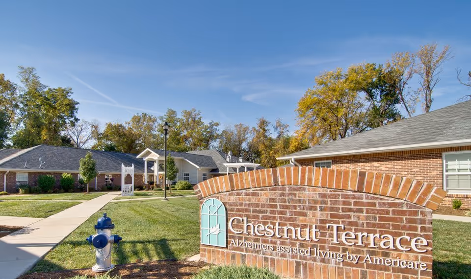 Brick entrance sign reading "Chestnut Terrace" in front of single-story senior living buildings with a walkway and lawn.
