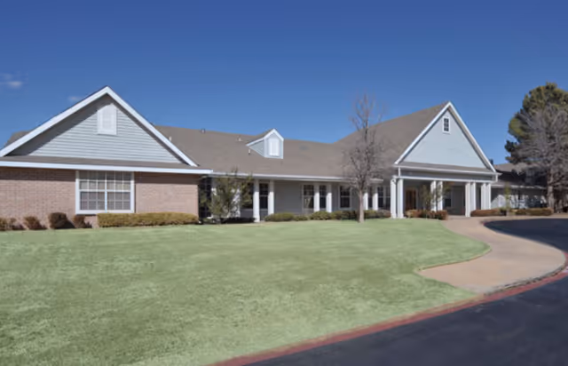 Single-story brick and siding senior living building with a covered entrance, front lawn, and driveway under a clear blue sky.