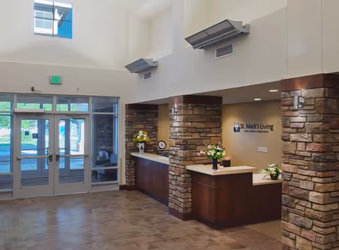 Interior lobby and reception area with stone pillars, front glass doors, and a wood reception desk with floral arrangements.