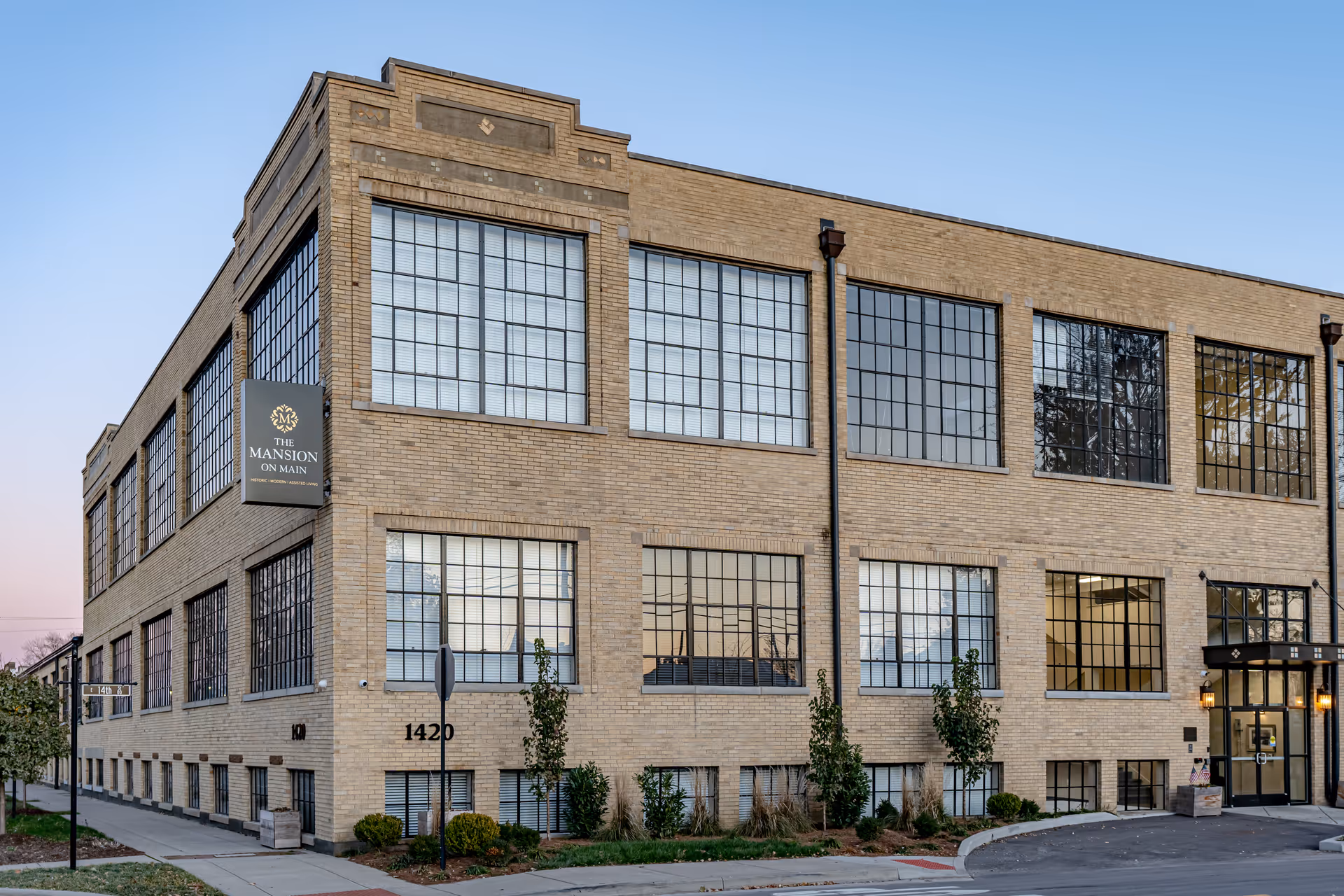 Exterior front of a two-story brick building with large industrial-style windows and a sign that reads "The Mansion on Main".